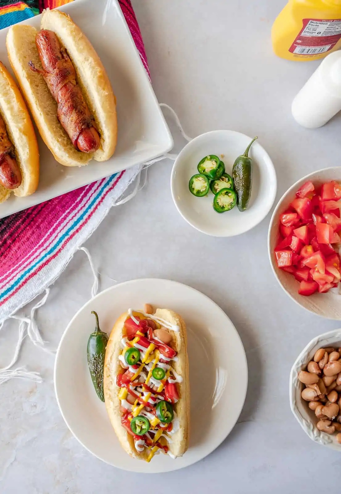Overhead view of plain Sonoran hot dogs on a plate and one with toppings.