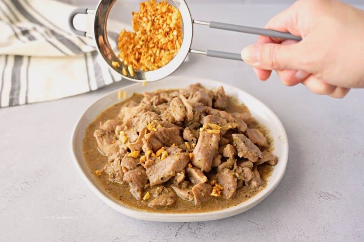 Adding fried garlic to a plate of cooked pork.
