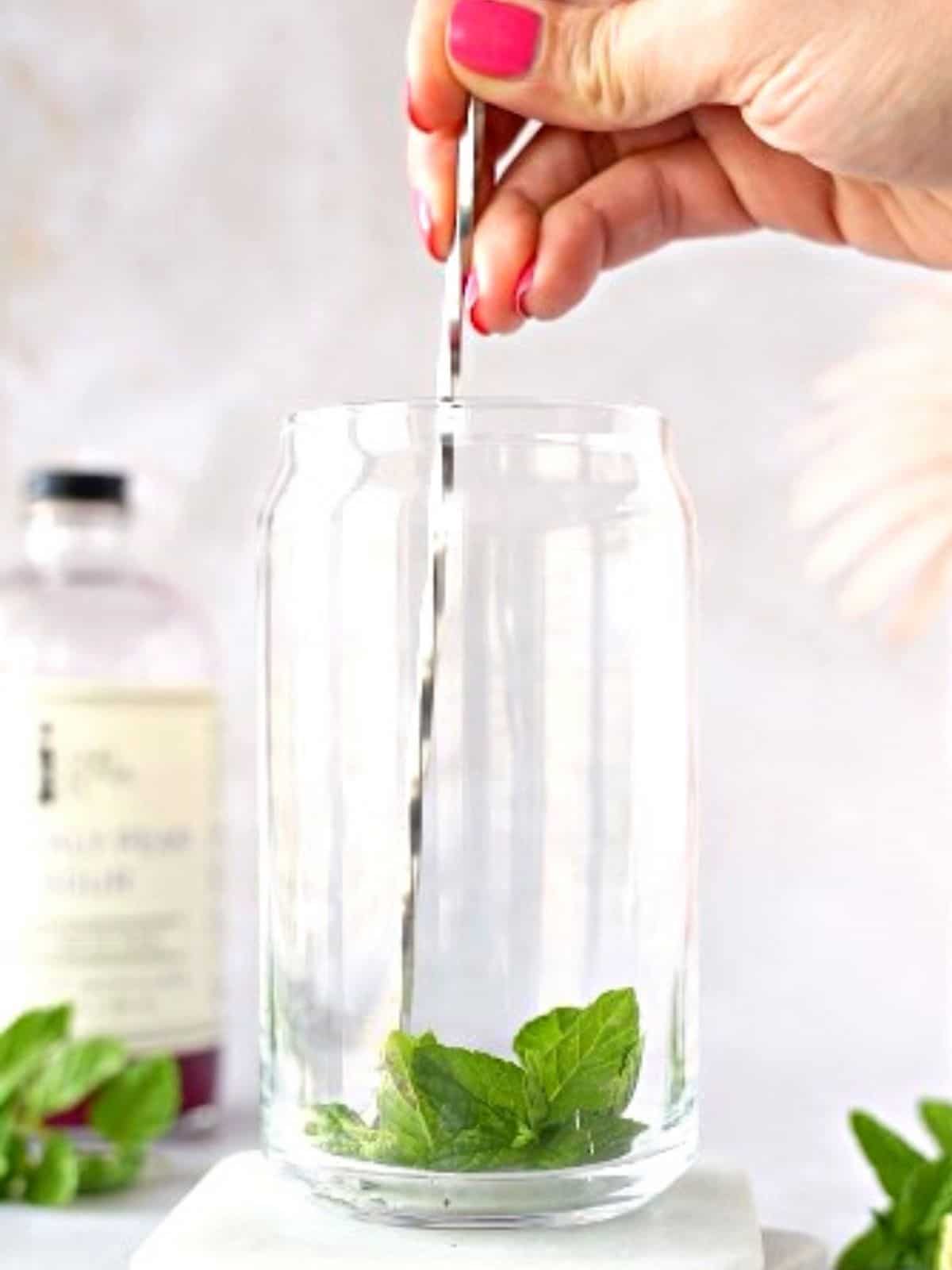 Mint being muddled in a glass.