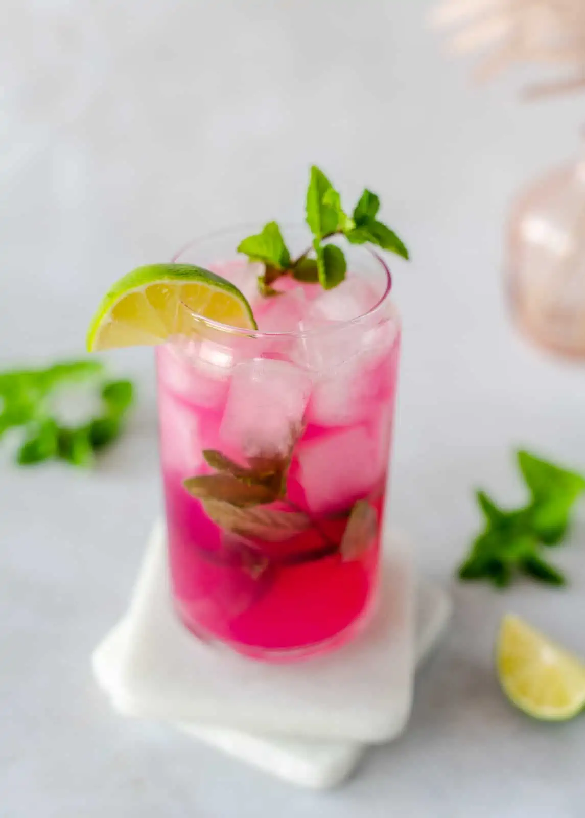 Pink cocktail garnished with mint and lime.