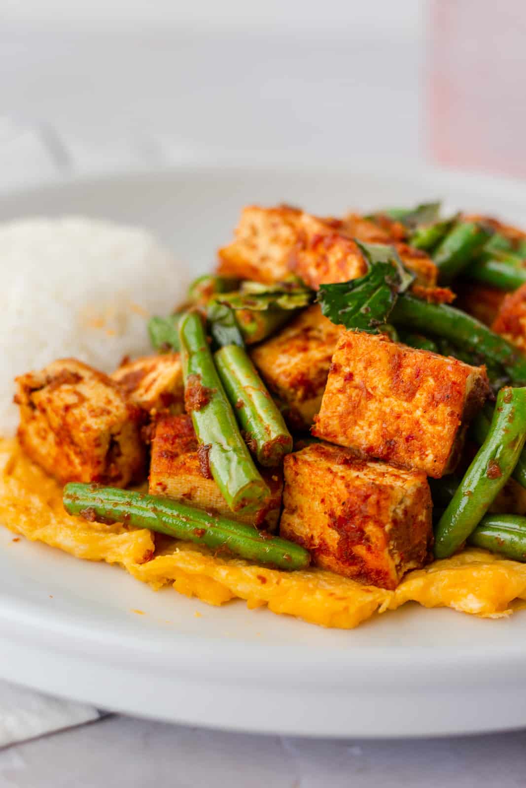 Red curry tofu stir fry on a plate with rice and egg on the bottom.