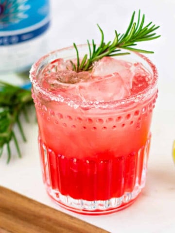 Red drink in a glass with a rosemary garnish.