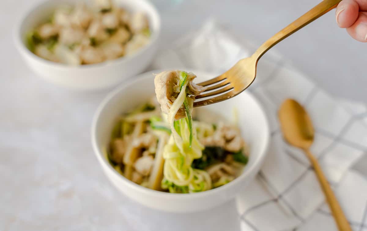 Fork holding zucchini noodles and chicken over bowl.