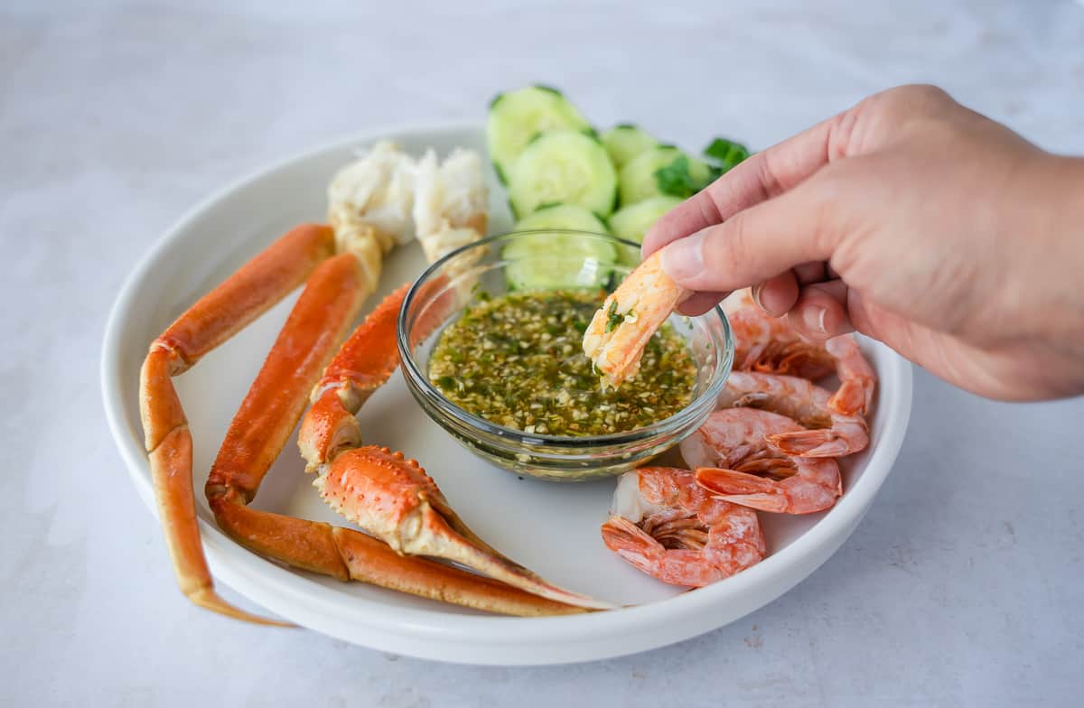 Hand holding a piece of crab being dipped into the sauce.