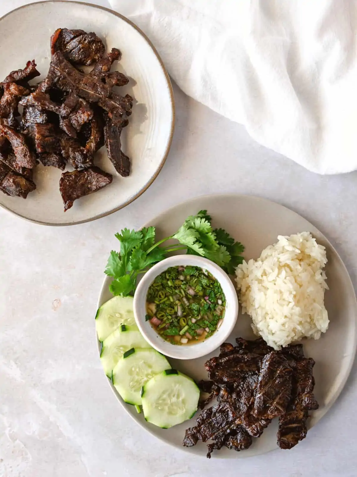 Overhead view of beef jerky on two plates with rice and cucumbers.