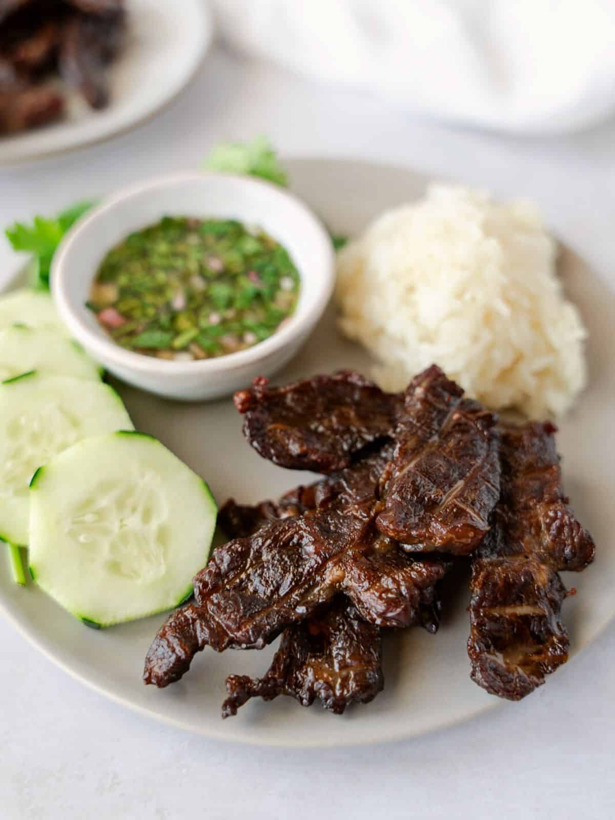 Cooked beef jerky on a plate with cucumber and sticky rice.