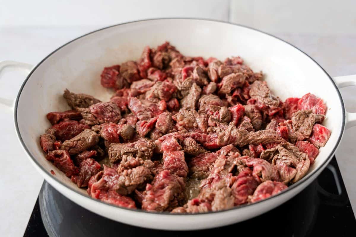 Beef cooking in a large white skillet.