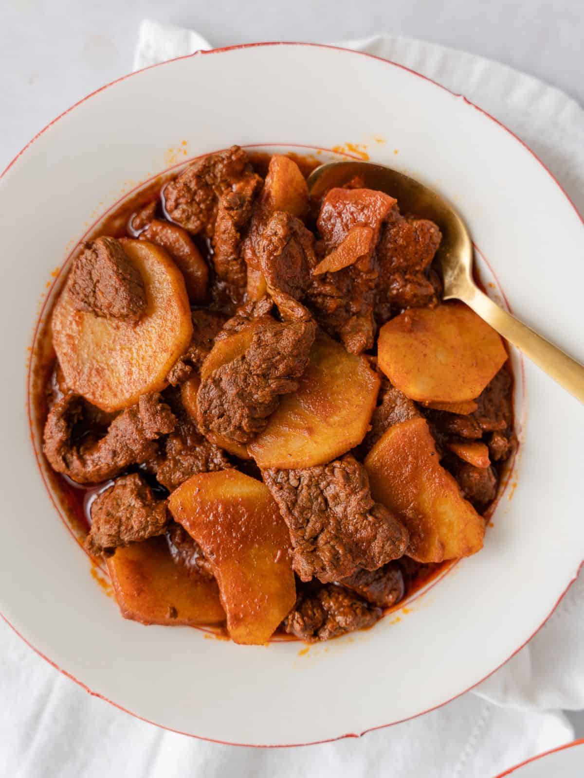 Beef and potatoes in a white bowl.