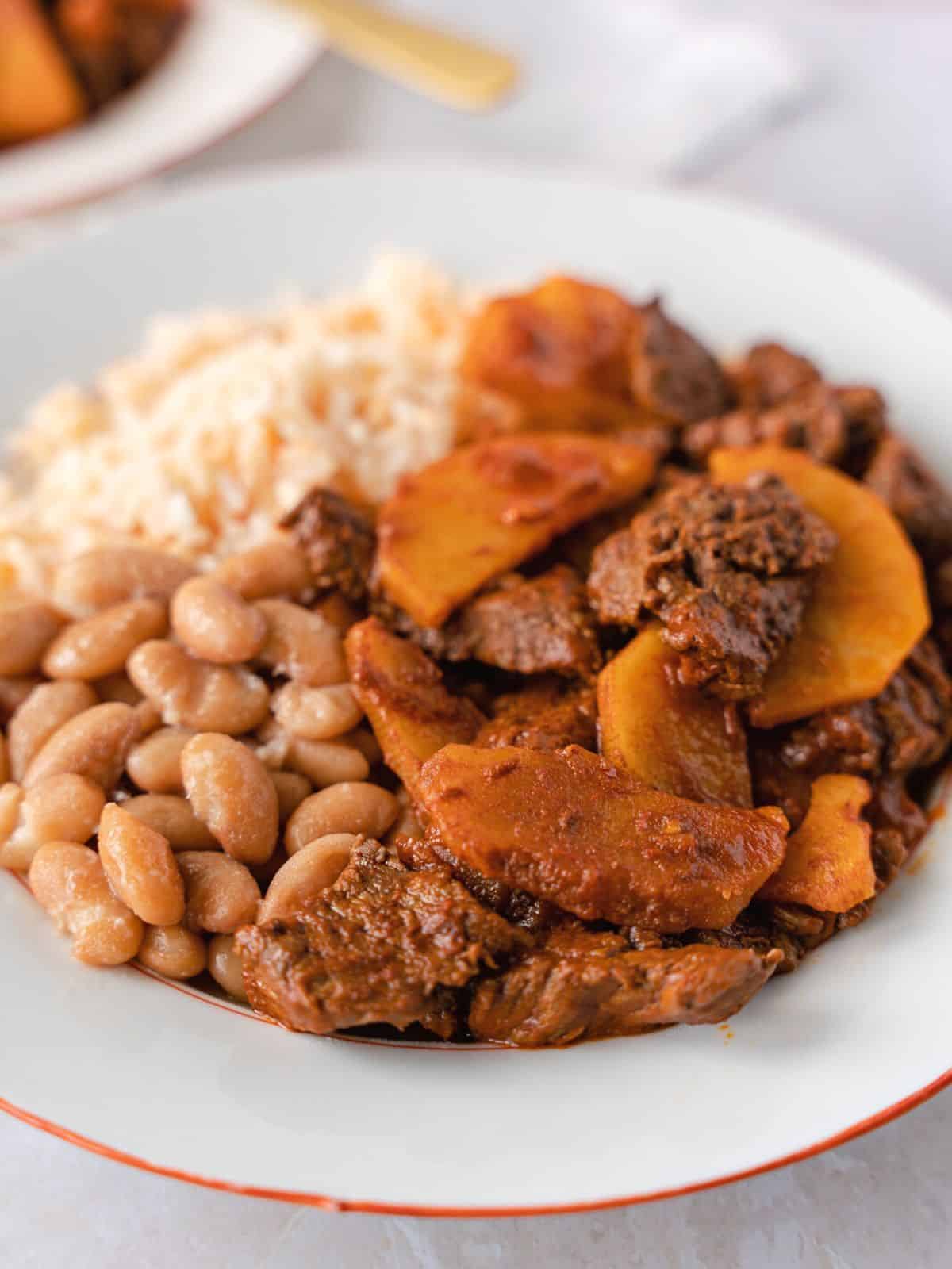 Beef and potatoes on a plate with rice and beans.