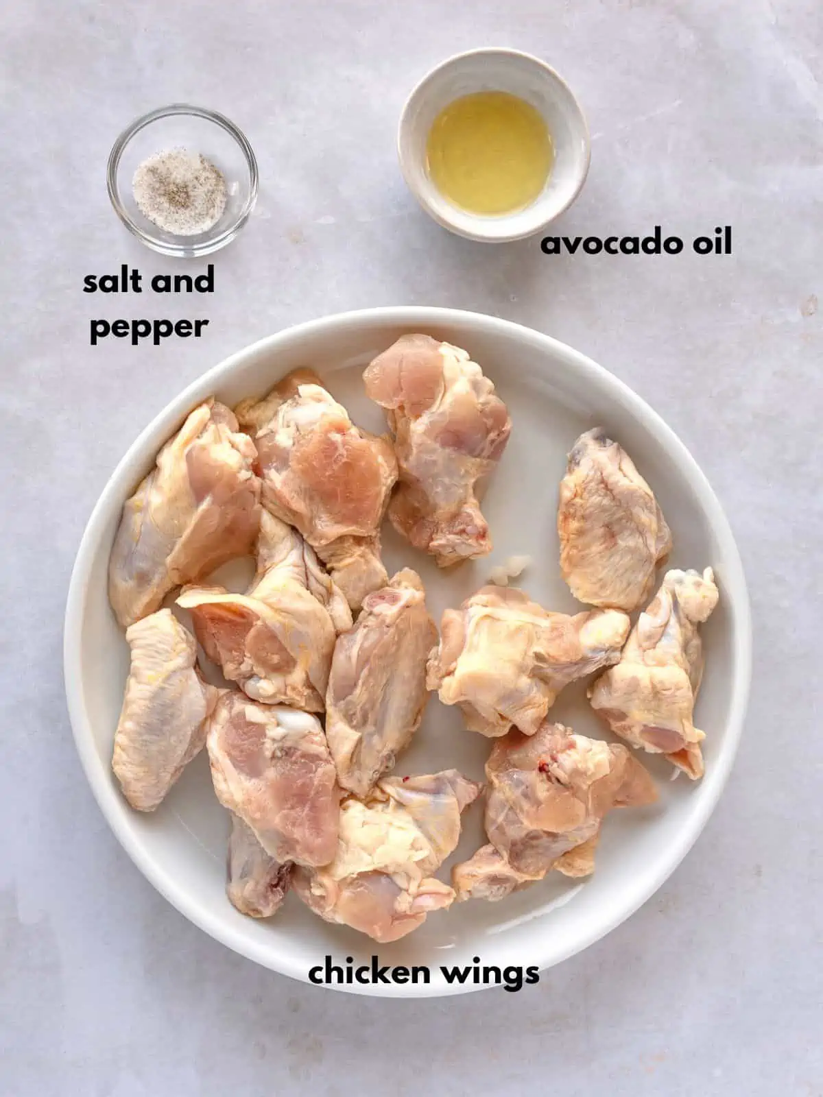 Raw chicken wings on a plate with avocado oil and salt and pepper in bowls.