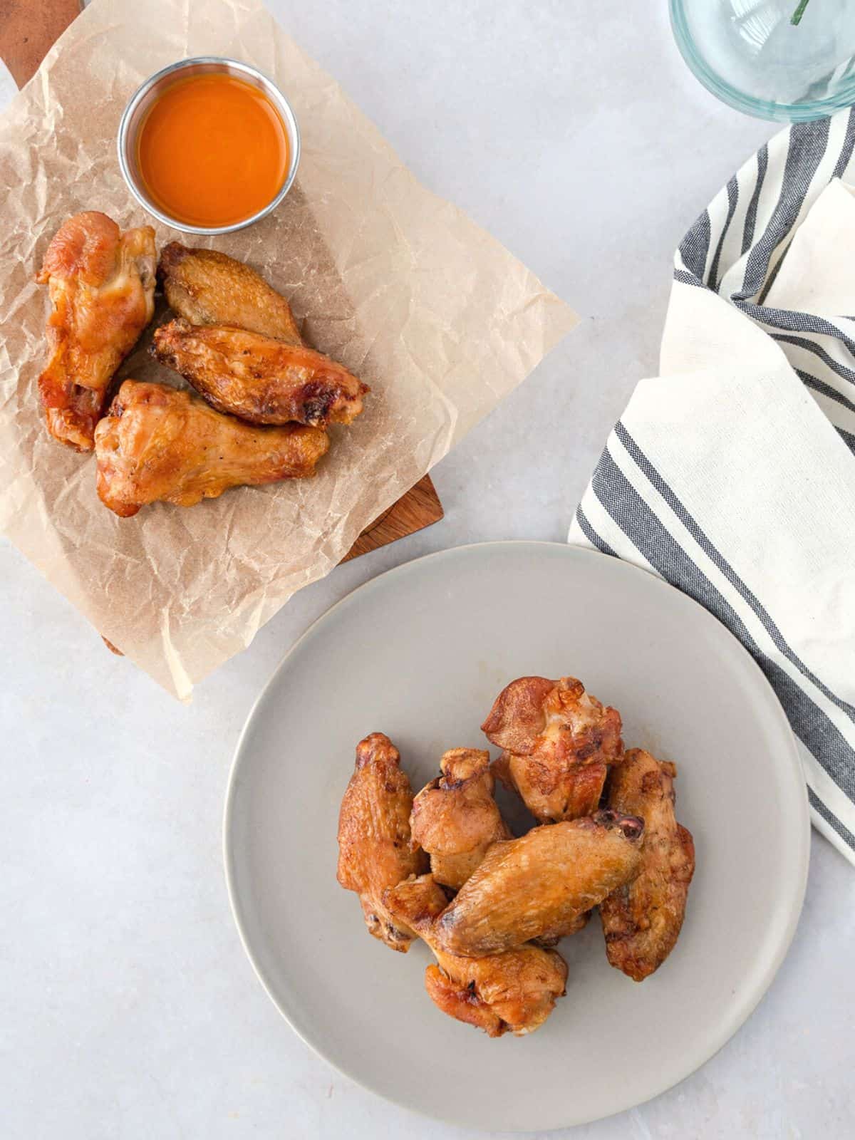 Overhead view of wings on a plate and board with buffalo sauce on the side.