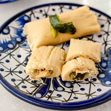 Feature image or 2 tamales de rajas con queso on a blue plate.