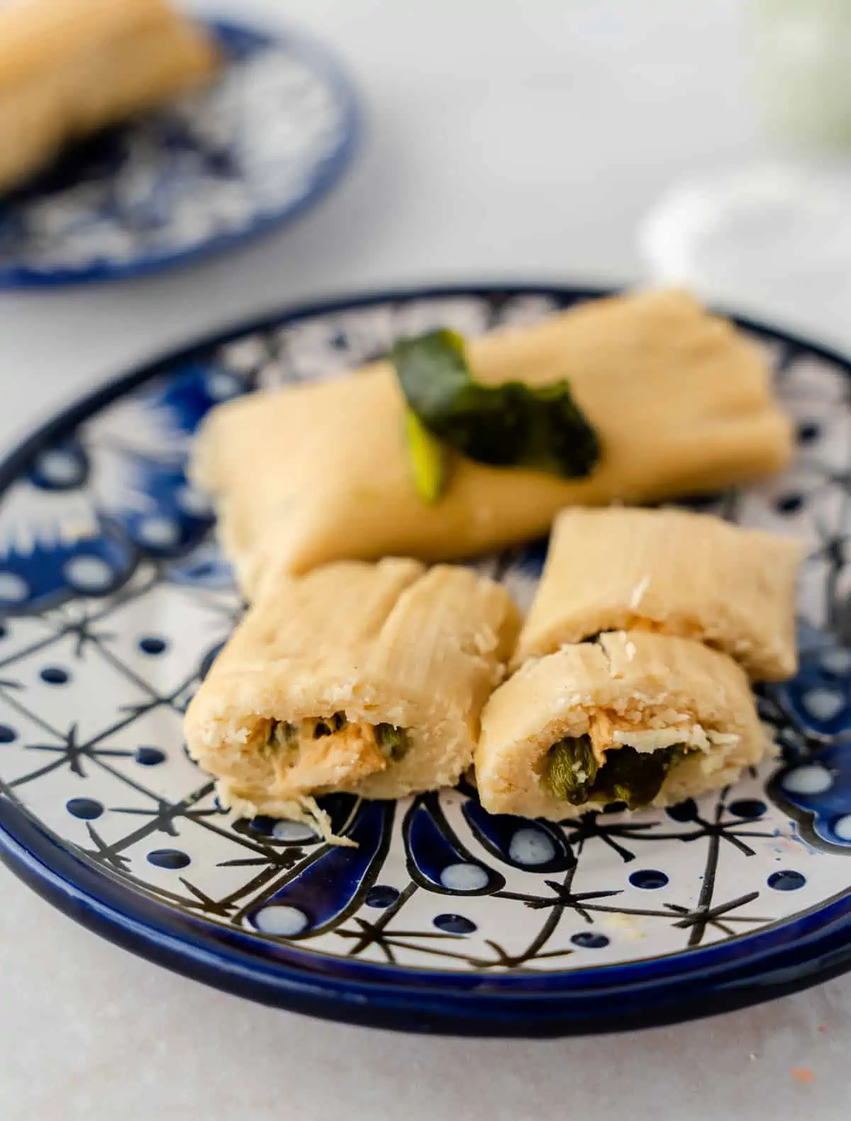 2 tamales on a plate with 1 cut open in half to see the filling.