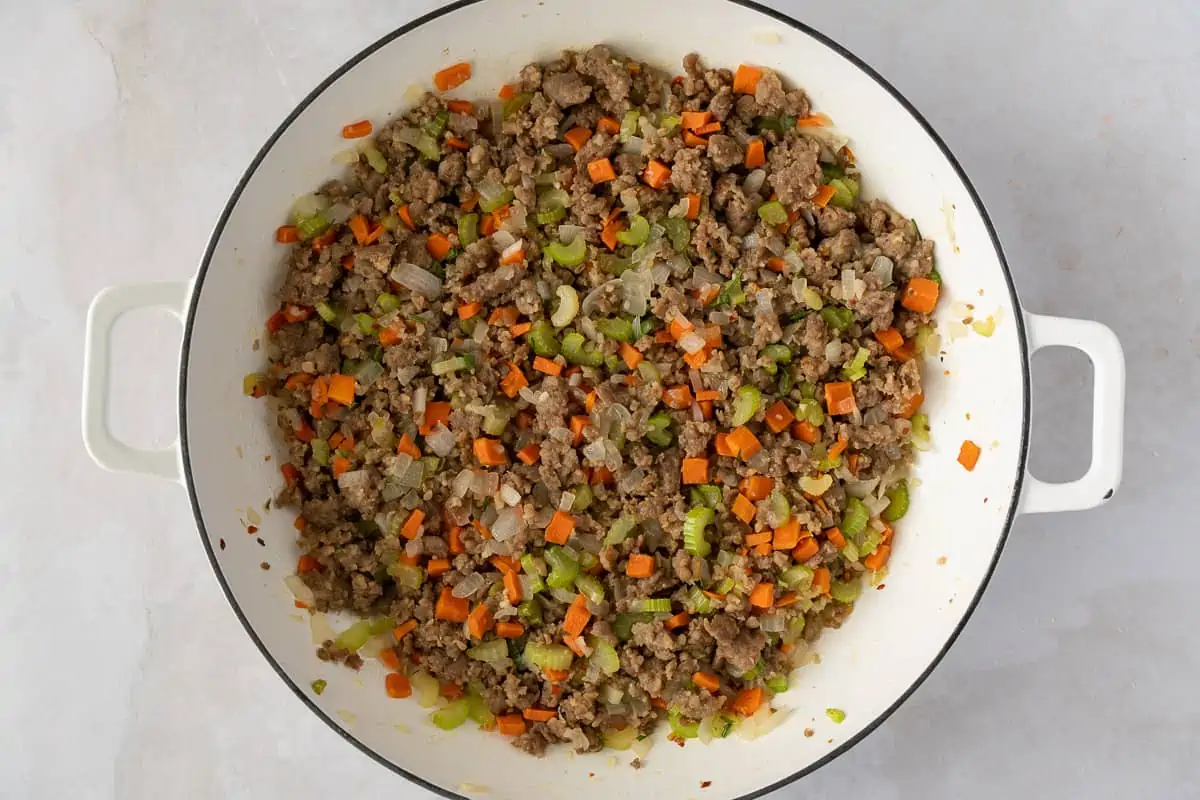 Cooked sausage, carrots, onions, and celery in a skillet.