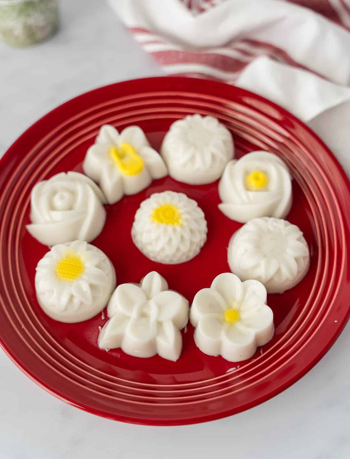 Coconut jelly desserts shaped in flowers on a red round plate.