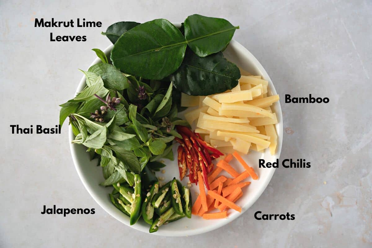 Lime leaves, bamboo, red chilis, carrots, jalapenos, and basil on a plate.