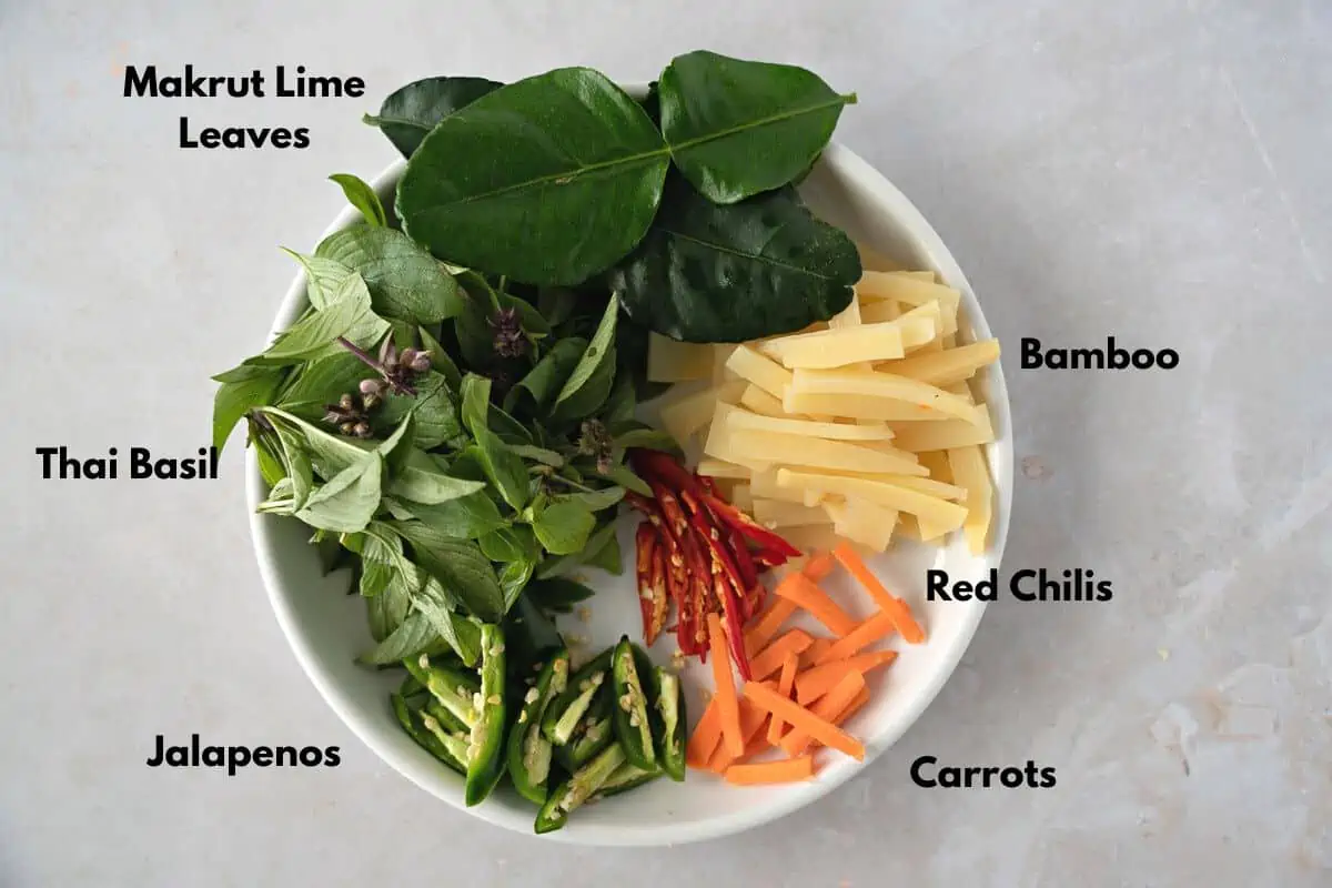 Lime leaves, bamboo, red chilis, carrots, jalapenos, and basil on a plate.