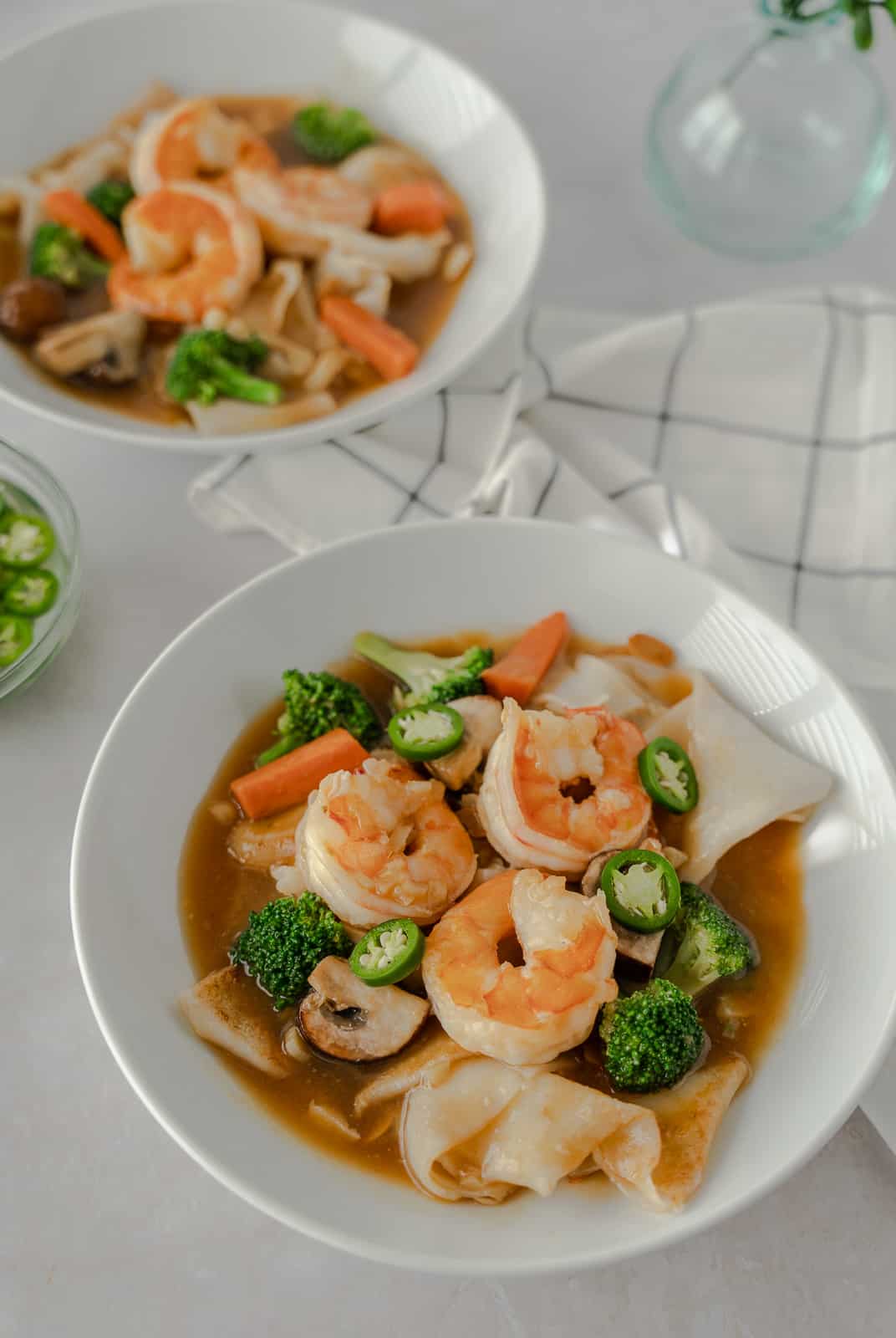 Two bowls of rice noodles with gravy and shrimp on top.