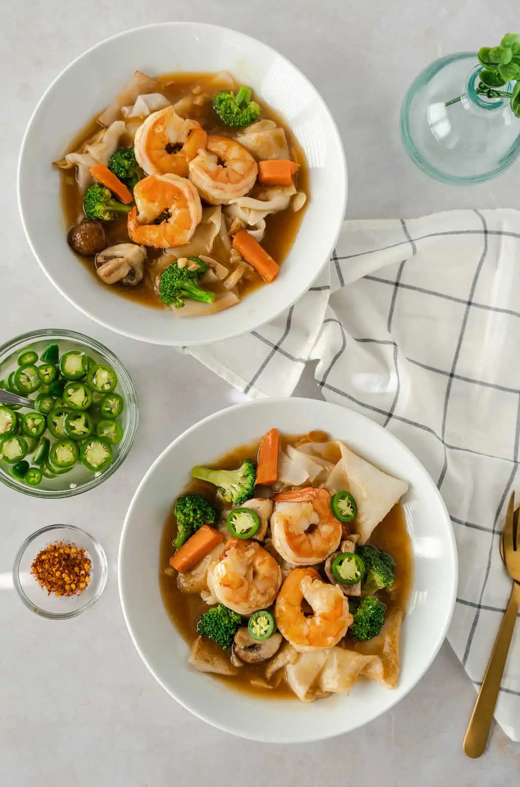 Overhead view of 2 bowls of noodles and a small bowl of chiles.