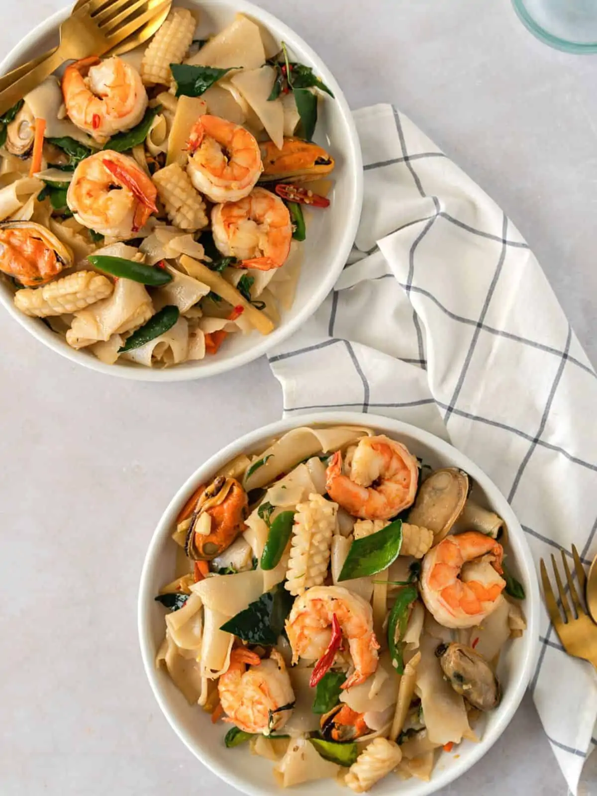 Overhead view of 2 plates with noodles and seafood.