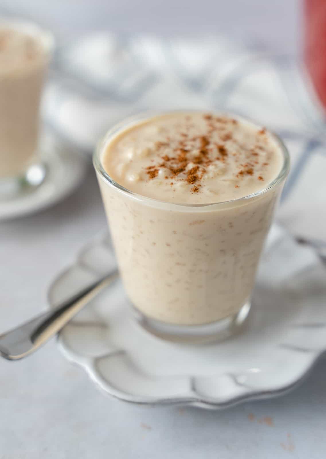 Rice pudding in a glass cup on a scalloped white plate.