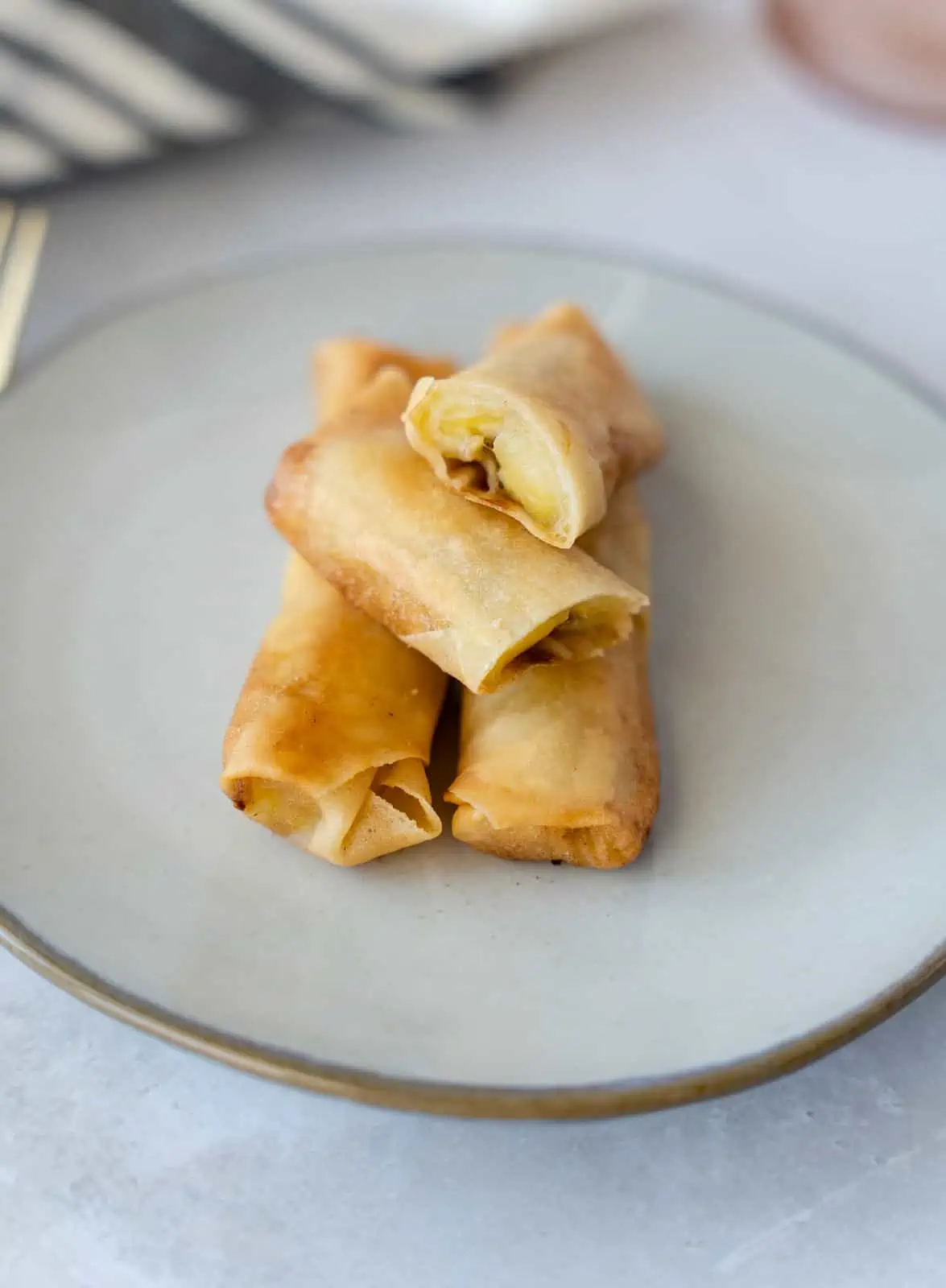 Fried Banana spring roll on a plate with one sliced in half.