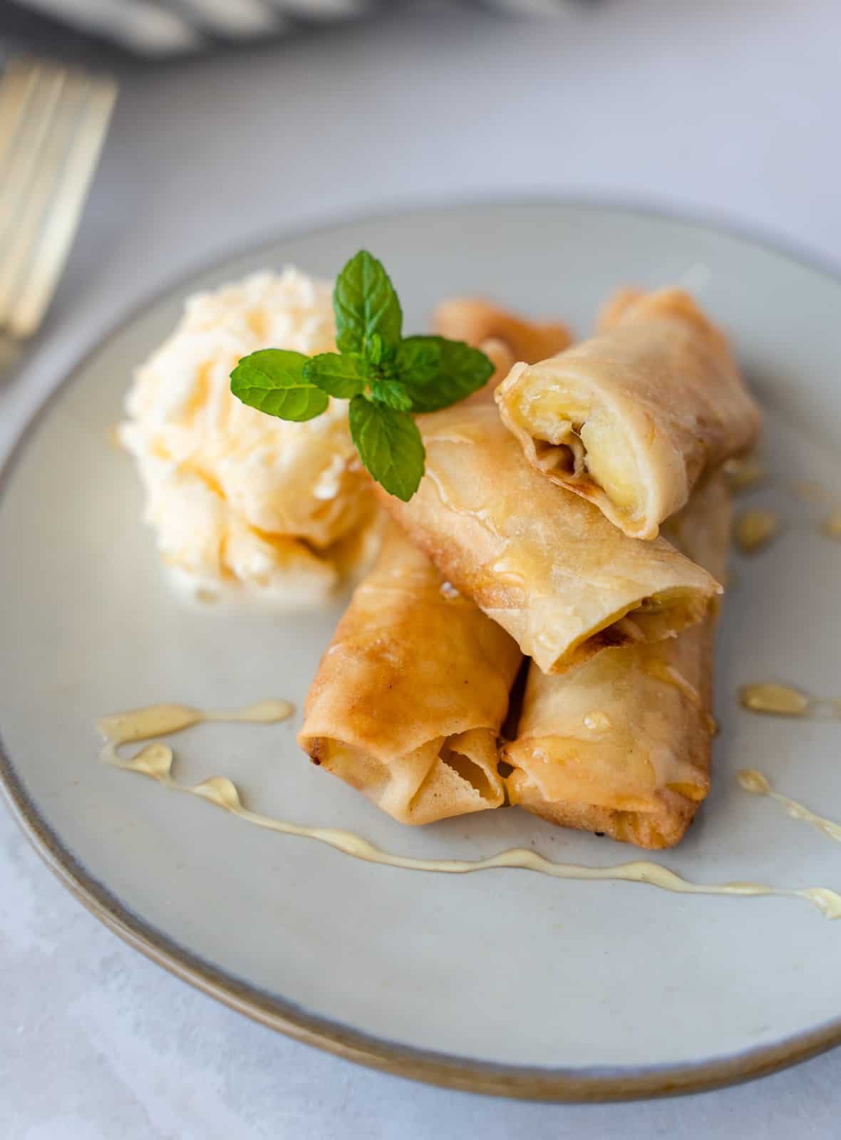 Banana spring rolls on a plate with ice cream and a mint sprig.