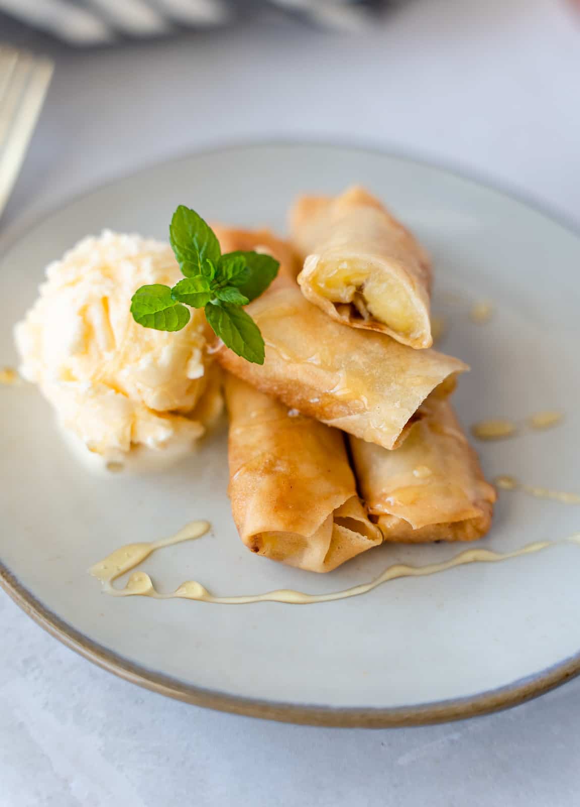 Fried banana rolls on a plate with ice cream and honey drizzled.