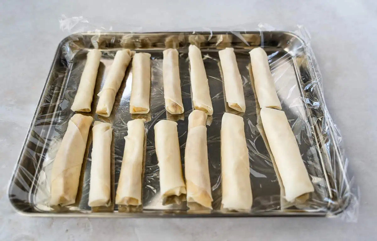 Rolled banana spring rolls on a plastic lined baking sheet.