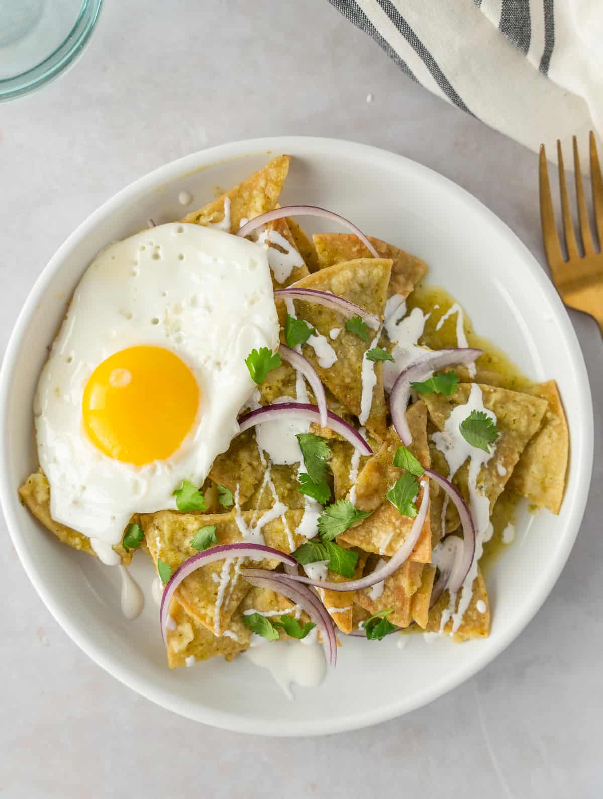 Overhead view of chilaquiles verdes con huevo on a plate garnished with crema, red onions, and cilantro.