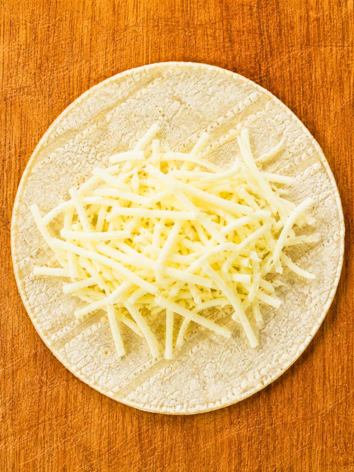 Shredded Monterey Jack cheese on a corn tortilla for Ground Beef Taquitos.