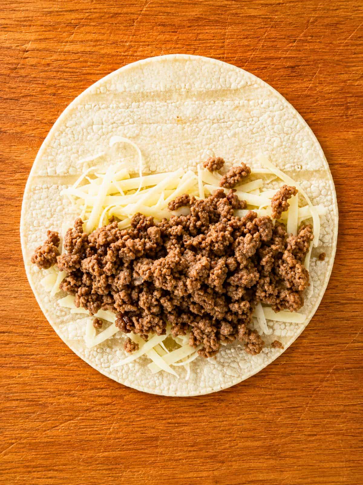 Seasoned ground beef and shredded cheese on a corn tortilla for Ground Beef Taquitos.
