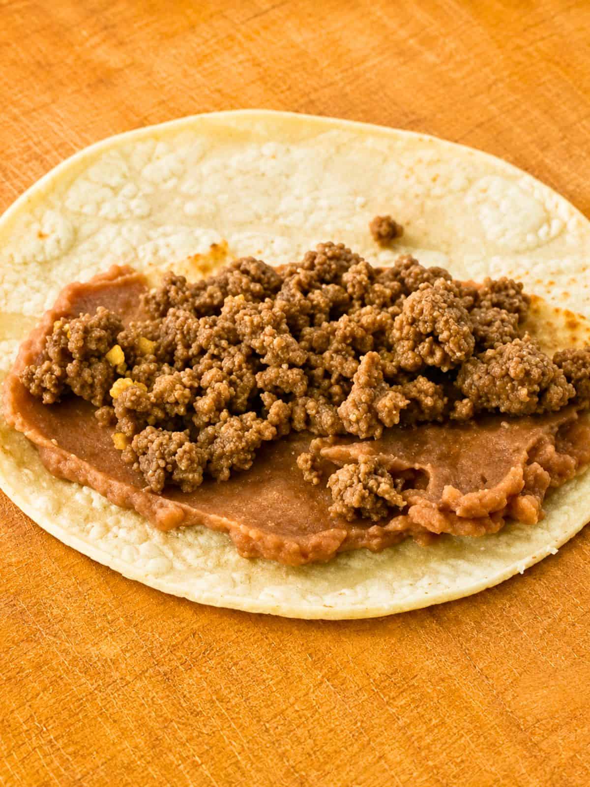 Refried beans and seasoned ground beef layered on a corn tortilla for Ground Beef Taquitos.