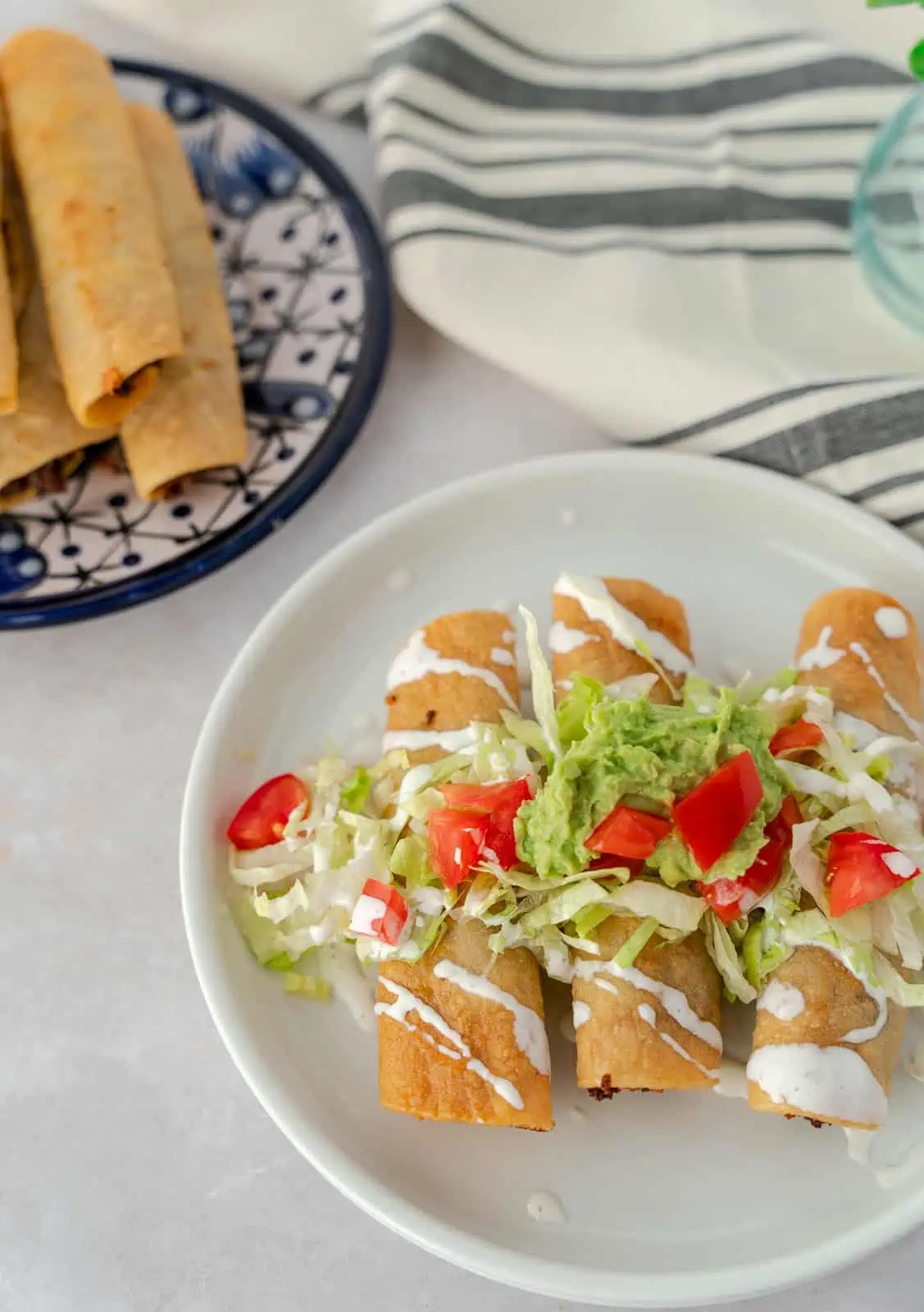 Plate with taquitos and toppings, and one plate without toppings.