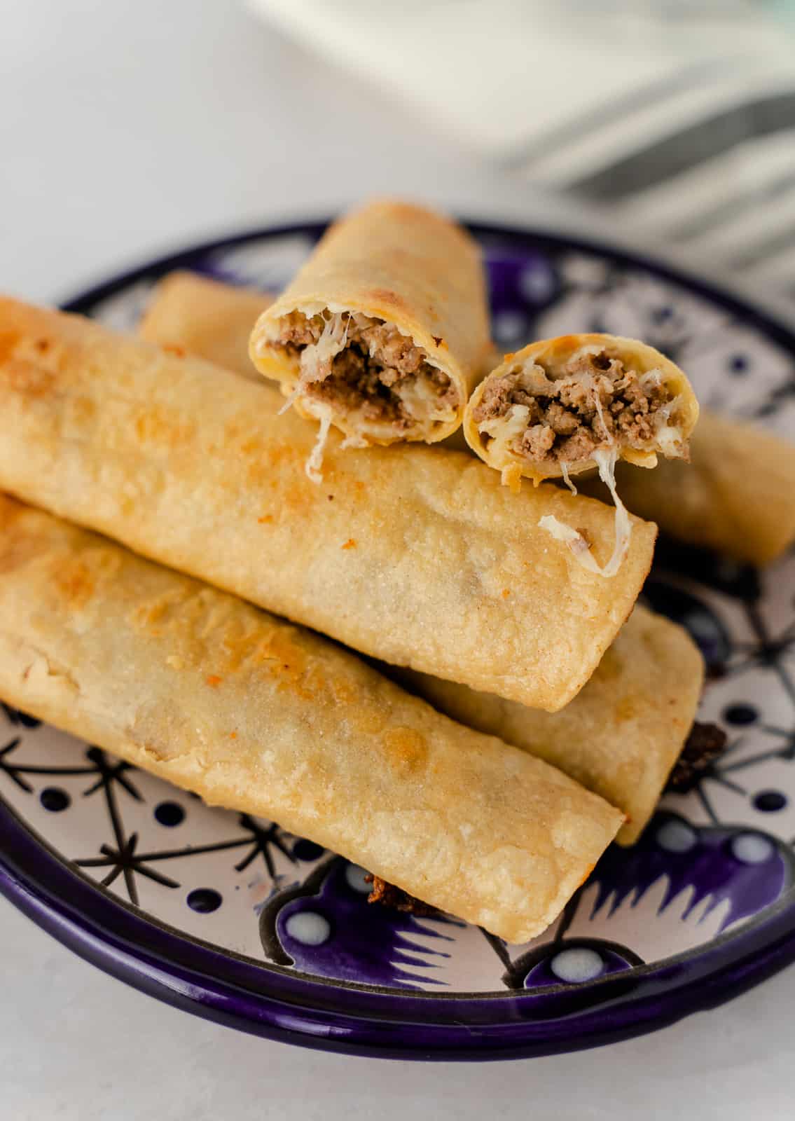 Fried ground beef taquitos on a plate with one cut in half.
