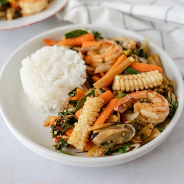 Seafood stir fry on a plate with a side of rice.