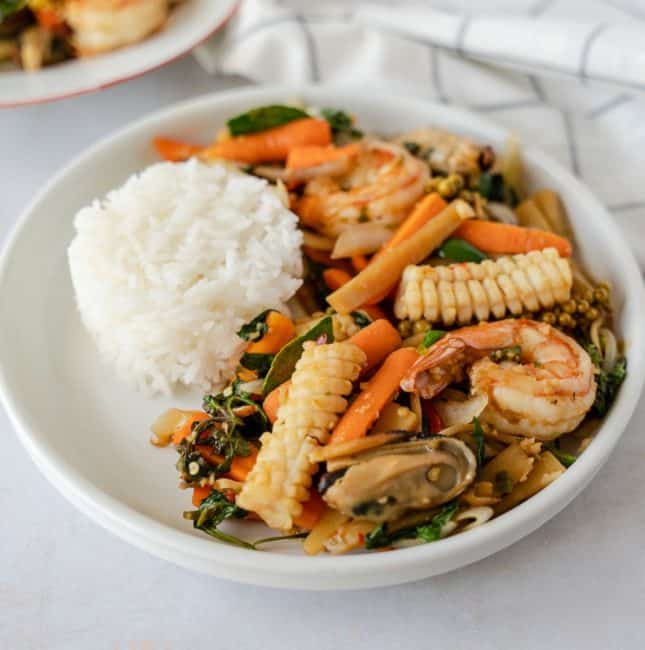Seafood stir fry on a plate with a side of rice.