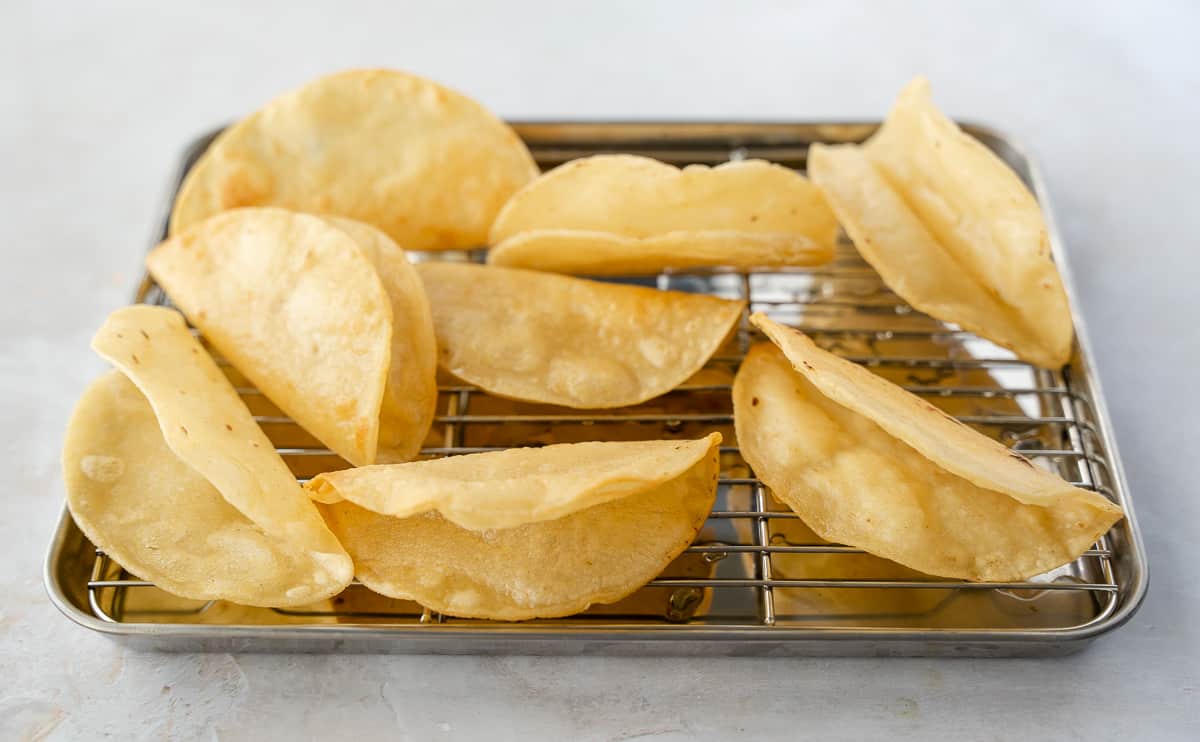 Fried tacos shells on a baking sheet.