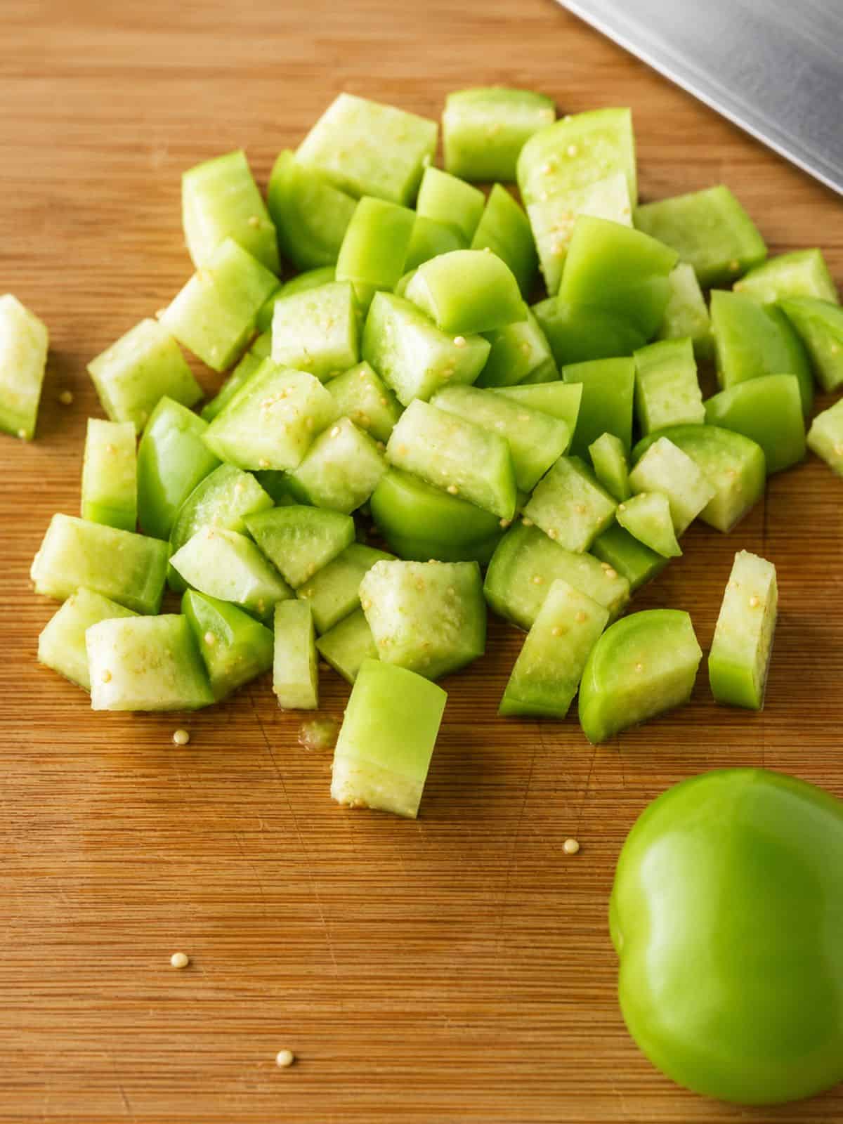 Fresh tomatillos diced on a wooden cutting board.