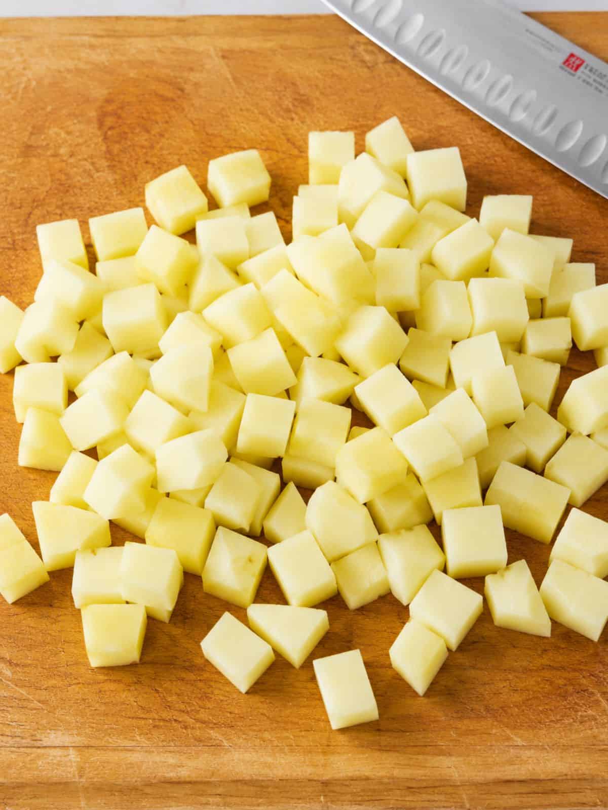 Peeled potato diced into small cubes on a wooden cutting board.