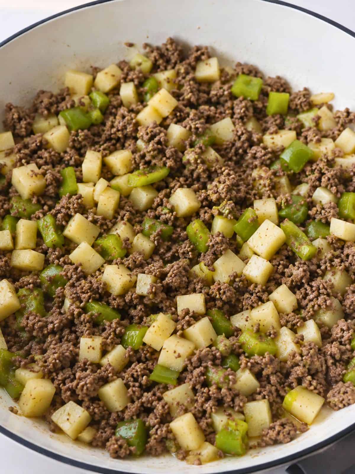 Mexican picadillo with ground beef, diced potatoes, and tomatillos cooking in a skillet.