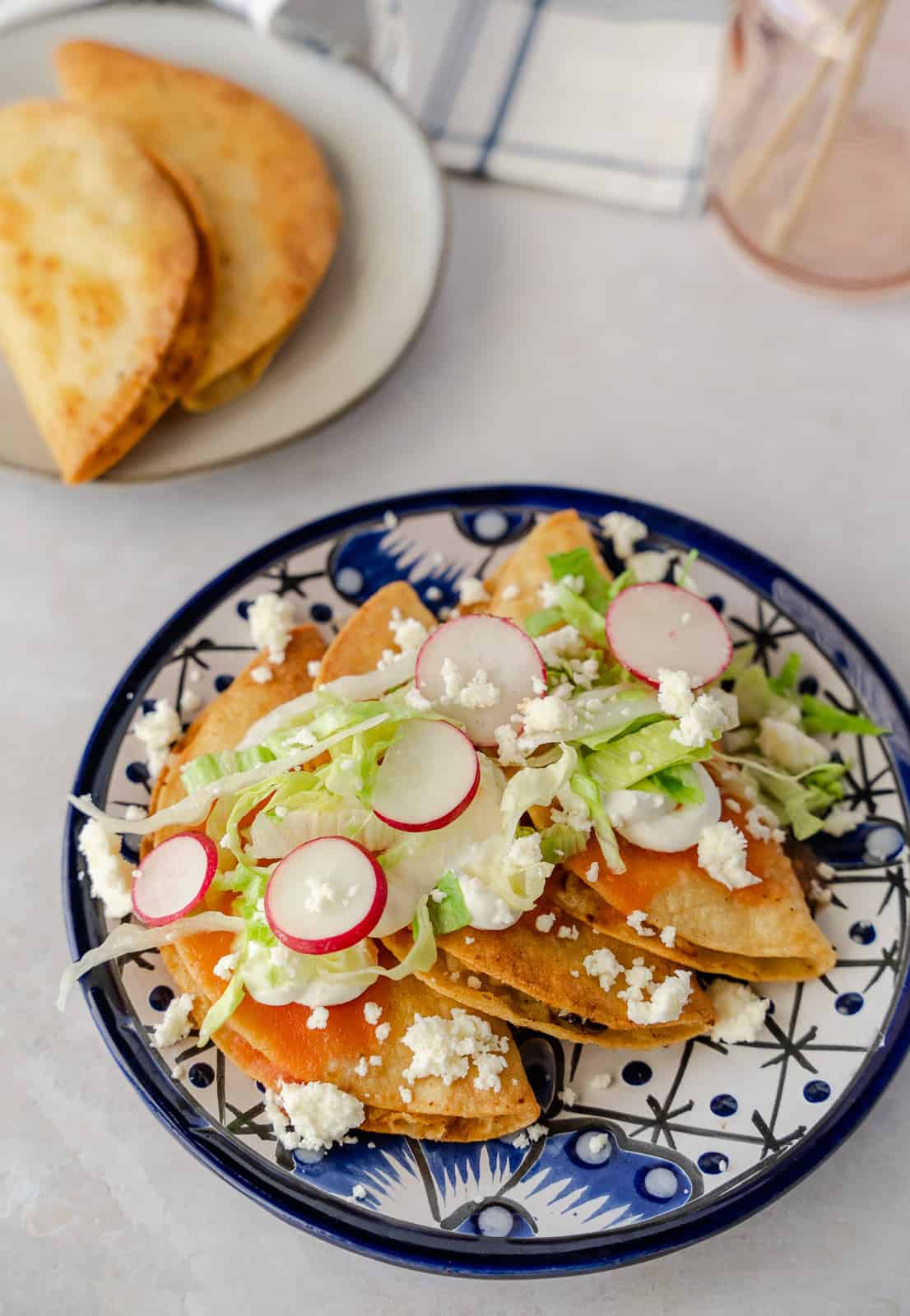 Two fried tacos on a small plate and 3 tacos with toppings on a bigger plate.