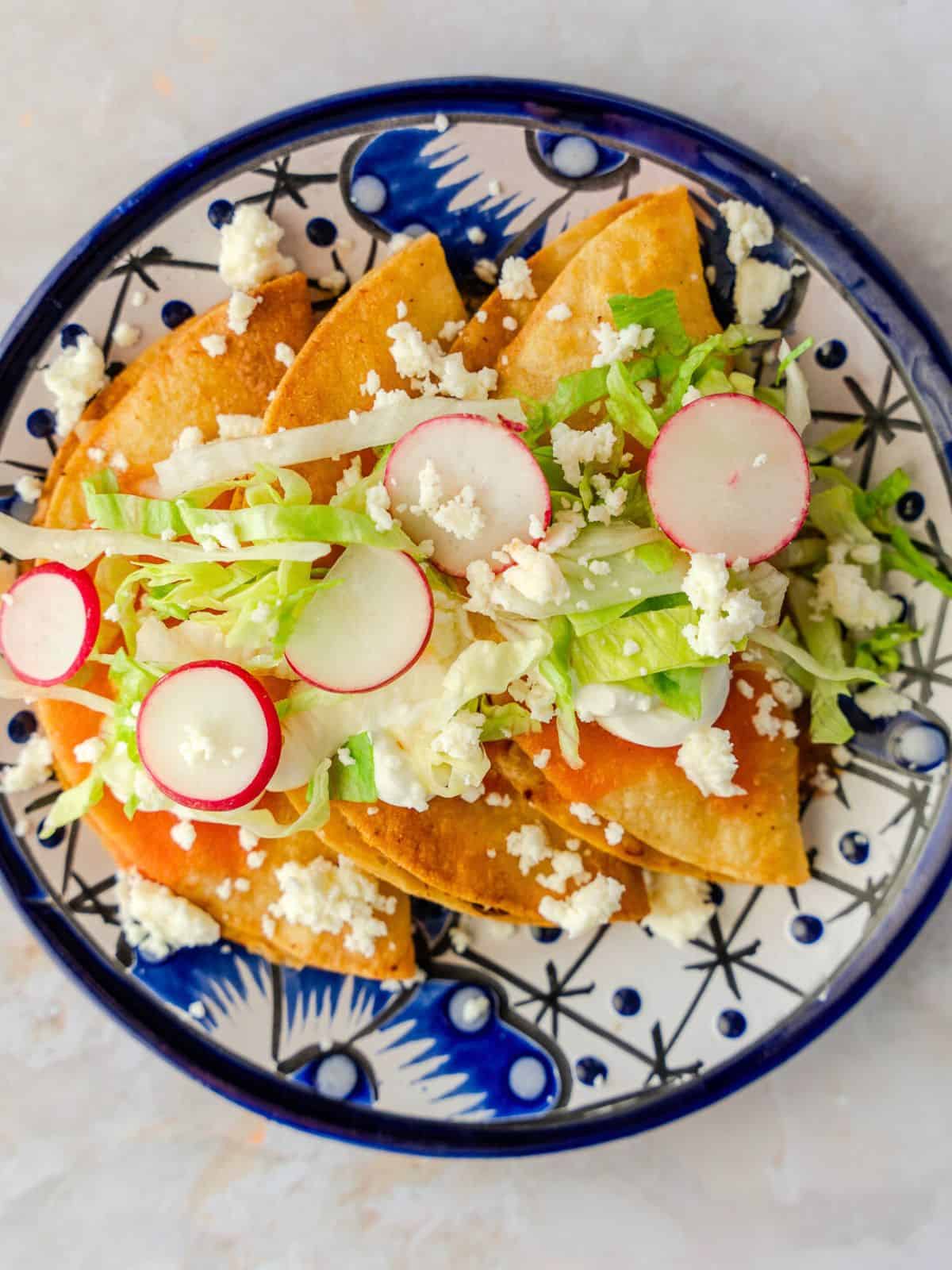 Tacos dorados on a blue plate with toppings.