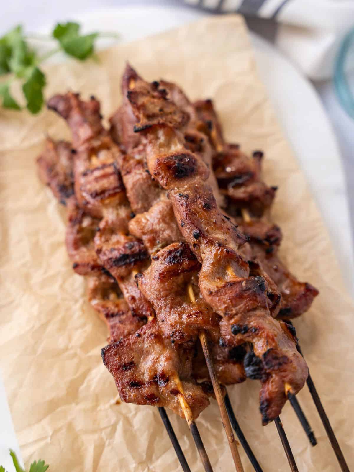 Grilled pork skewers on parchment paper with some cilantro garnish.