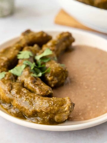 Feature image of costillas en salsa verde on a plate with beans.