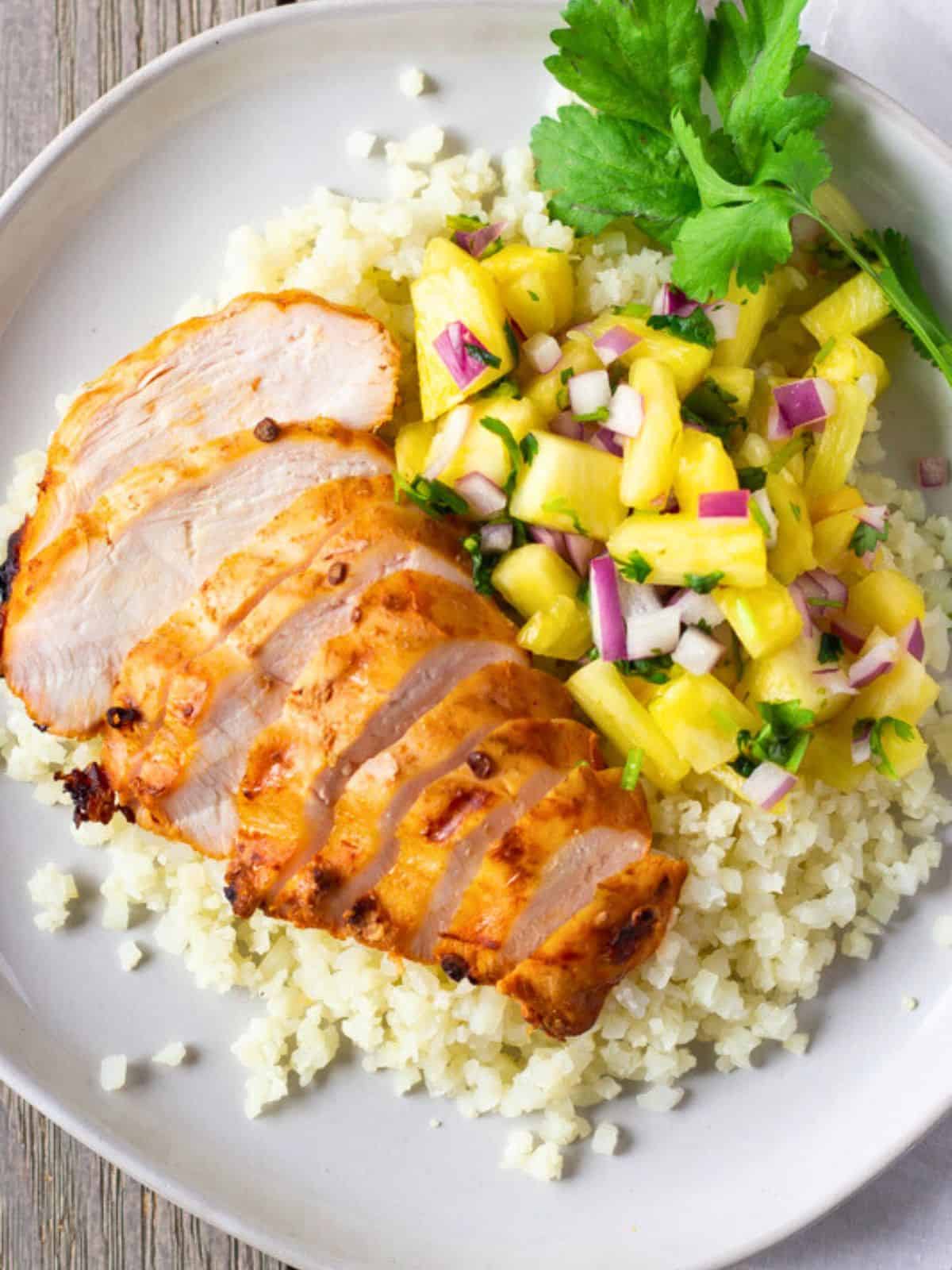 Sliced chicken on a plate with cauliflower rice and pineapple salsa.