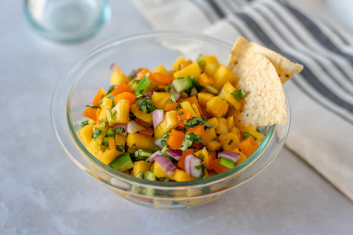 Mango salsa in a glass bowl with a few tortilla chips on the side.