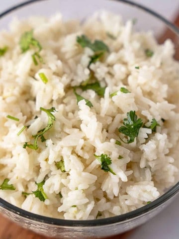 Feature image of coconut lime rice in a glass bowl topped with cilantro.