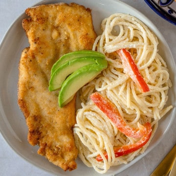 Chicken Milanese on a plate with white pasta and sliced avocado.
