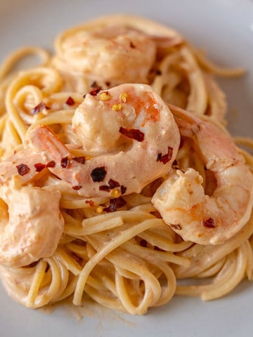 Four pieces of shrimp on pasta garnished with red pepper flakes.
